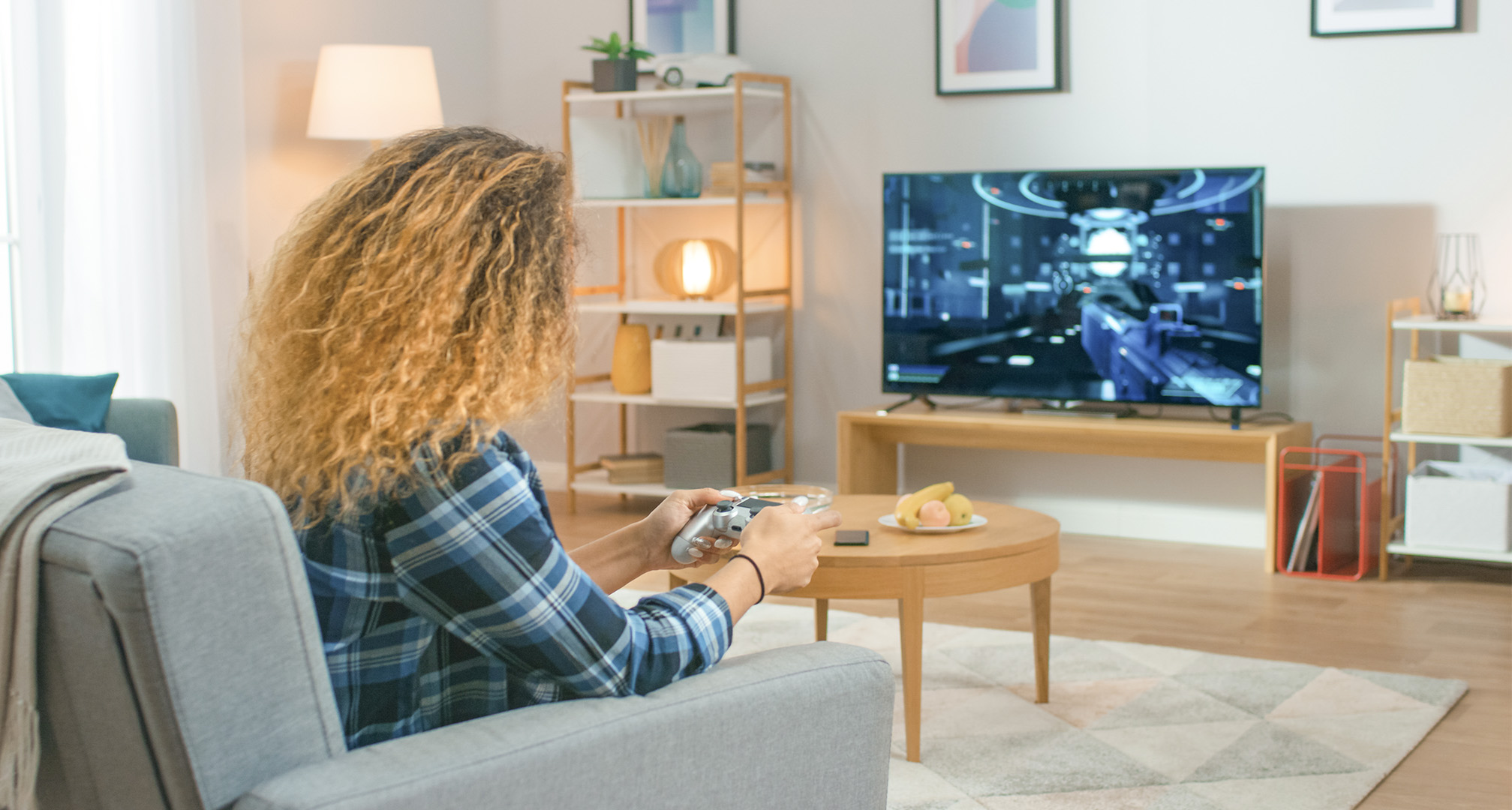 person med langt krøllet hår i stuen, der spiller computerspil på en tv-skærm