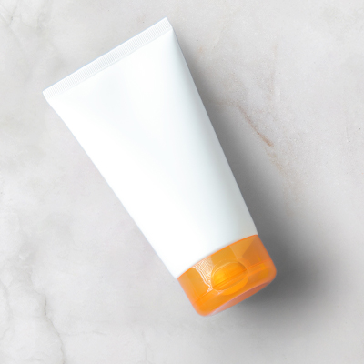 hvid tube med solcreme med orange hætte på neutral baggrund